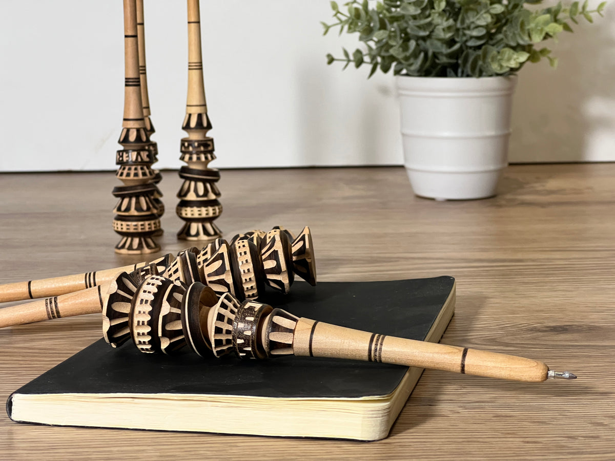 Wooden pen with black and natural geometric patterns and woven bristle detail at the barrel.