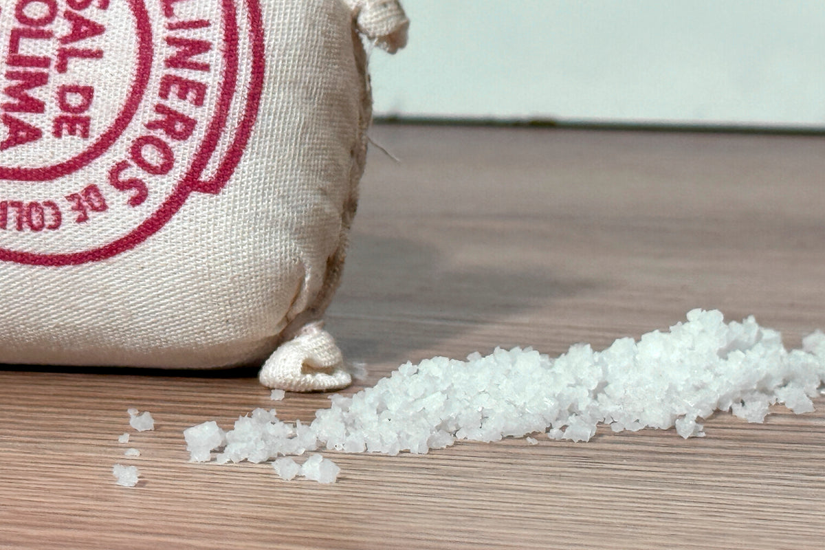 Cream canvas bag with red circular stamp next to pile of white sea salt crystals on wooden surface.