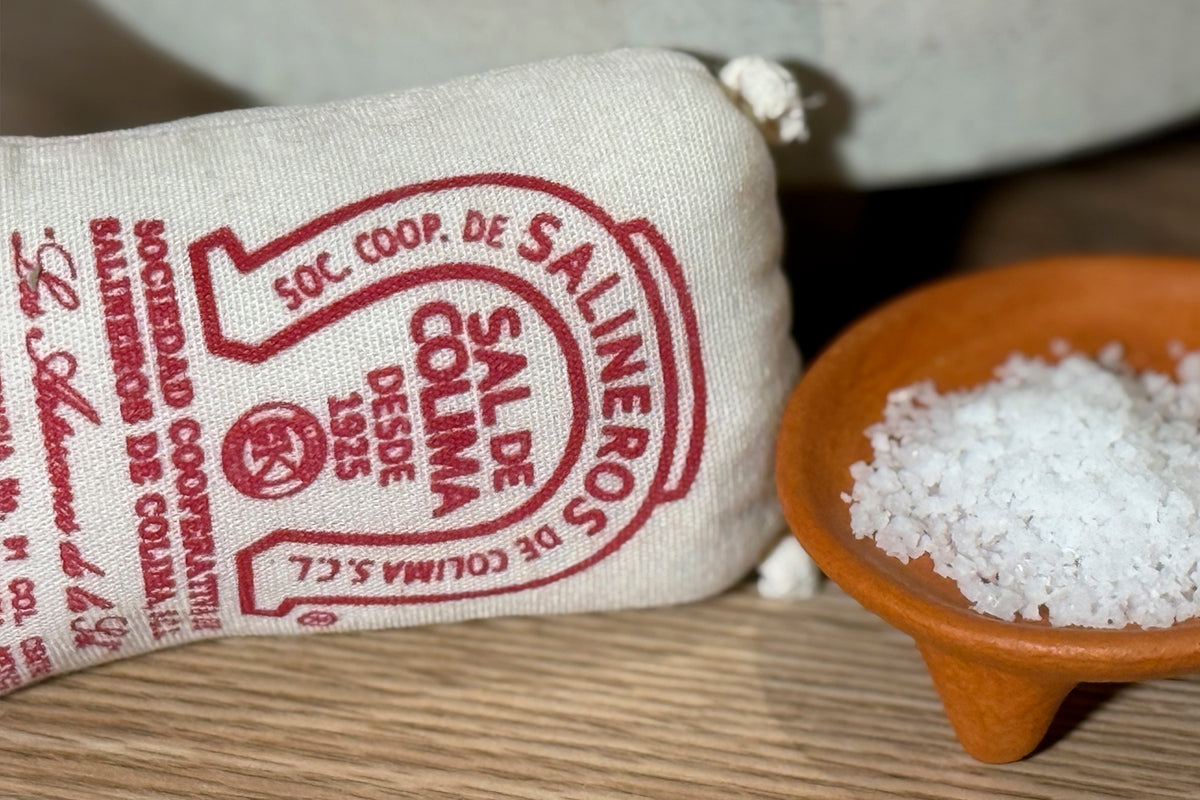 Colima sea salt in terracotta bowl next to cloth bag with red text and seal.