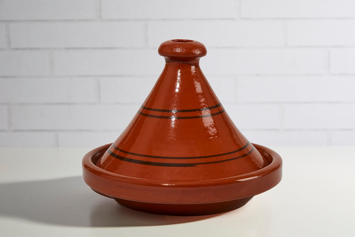 Red ceramic tagine with cone-shaped lid, black decorative stripes, and matching round base bowl.
