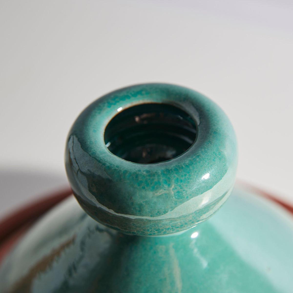 Turquoise ceramic tagine with conical lid and dark interior opening, showing glazed finish and textured surface.
