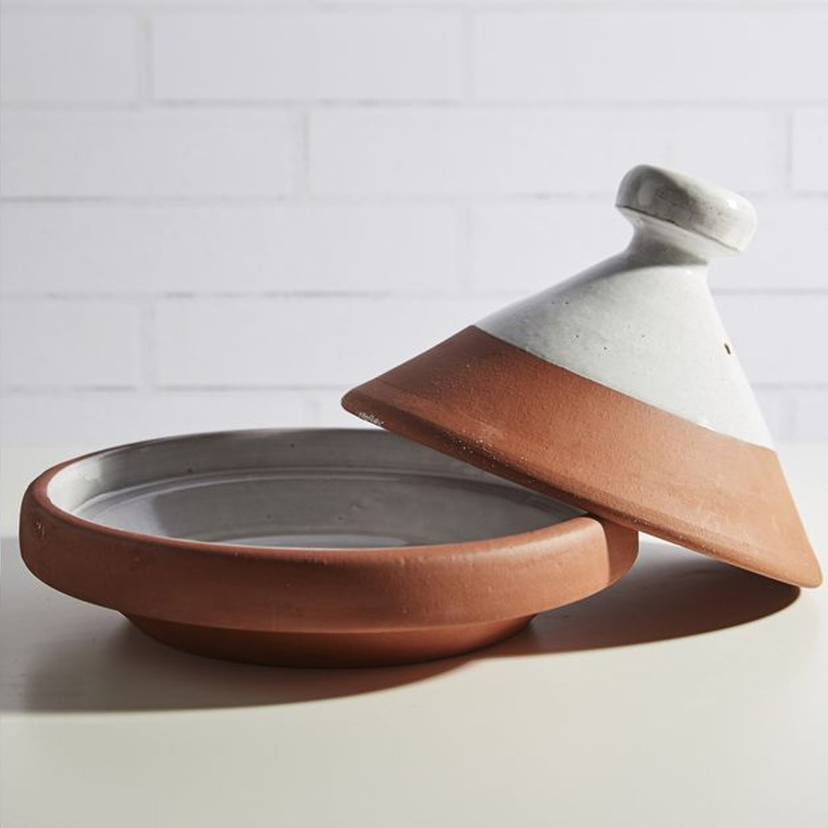Terracotta and cream ceramic tagine with conical lid and wide shallow base for cooking.