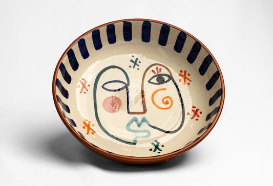 Ceramic bowl with cream-colored interior featuring hand-painted abstract face and geometric patterns in blue, orange, and red