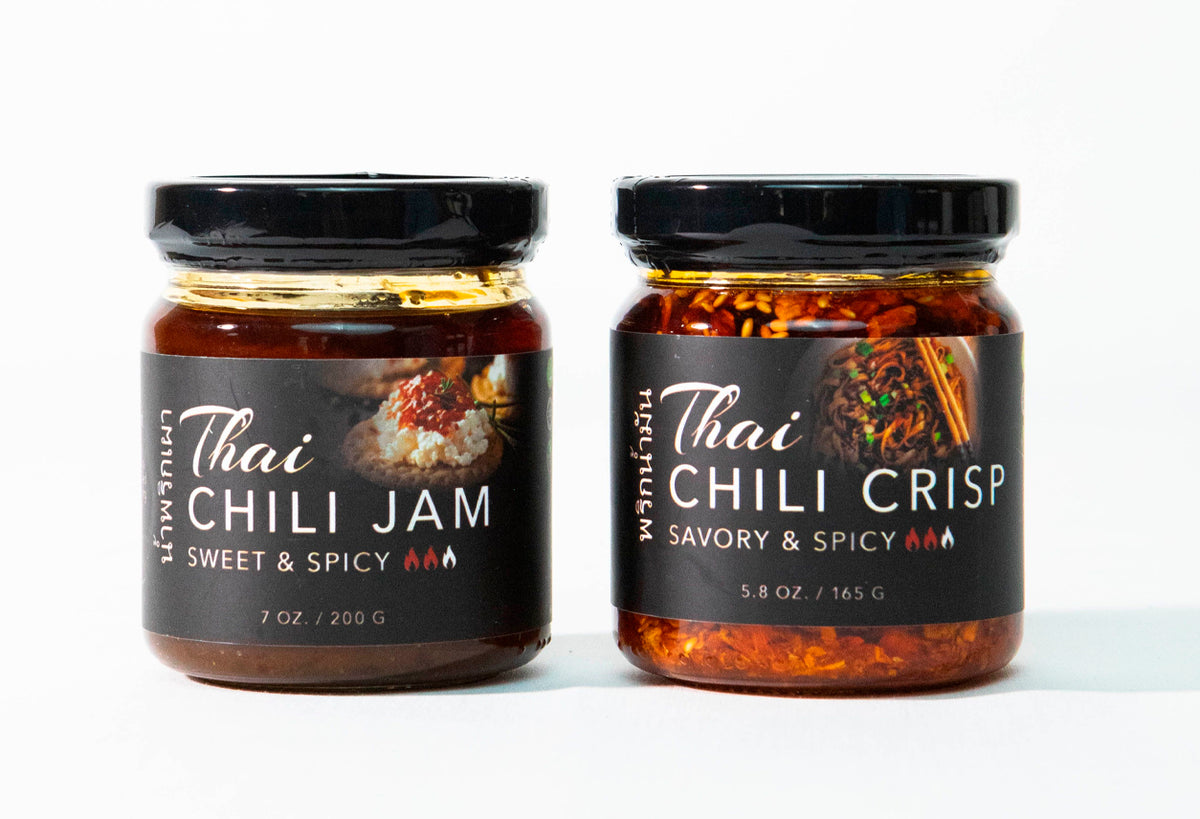 Two glass jars with black lids containing Thai chili jam and chili crisp with dark labels.