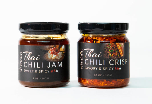 Two glass jars with black lids containing Thai chili jam and chili crisp with dark labels.