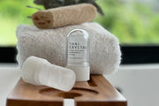 Two white Thai Crystal deodorant stones with applicators displayed on wooden surface with towels.