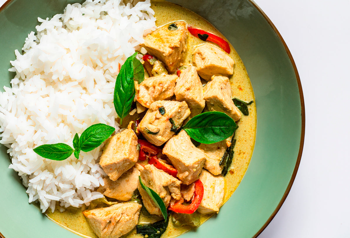 White jasmine rice served alongside curry with tofu, red peppers, and basil on green plate.