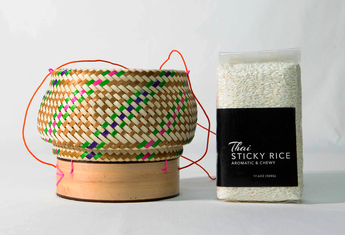 Woven rattan basket with colorful diamond pattern, wooden base, and orange handles, displayed next to package of Thai sticky 