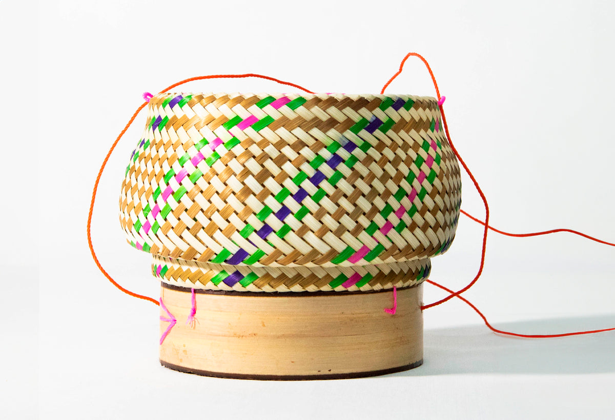 Woven bamboo rice basket with colorful geometric patterns and orange rope handles.