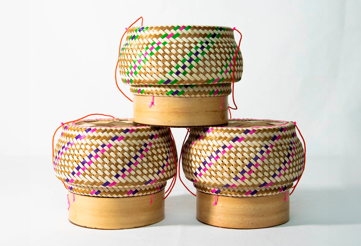 Woven straw baskets with wooden bases and colored thread patterns, featuring rope handles in coral and pink.