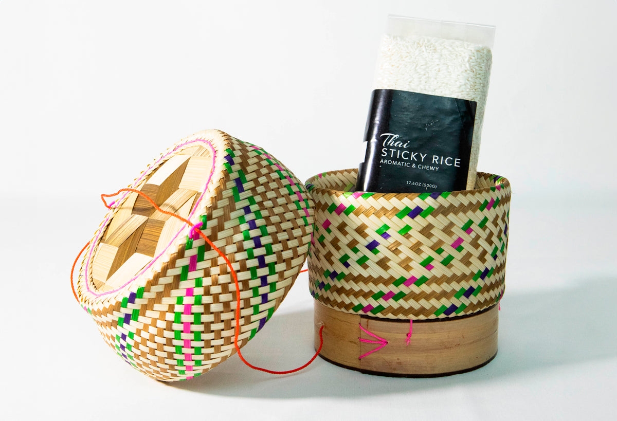 Woven bamboo serving baskets with colorful diamond pattern and pink cord trim, one open with lid and one holding rice package