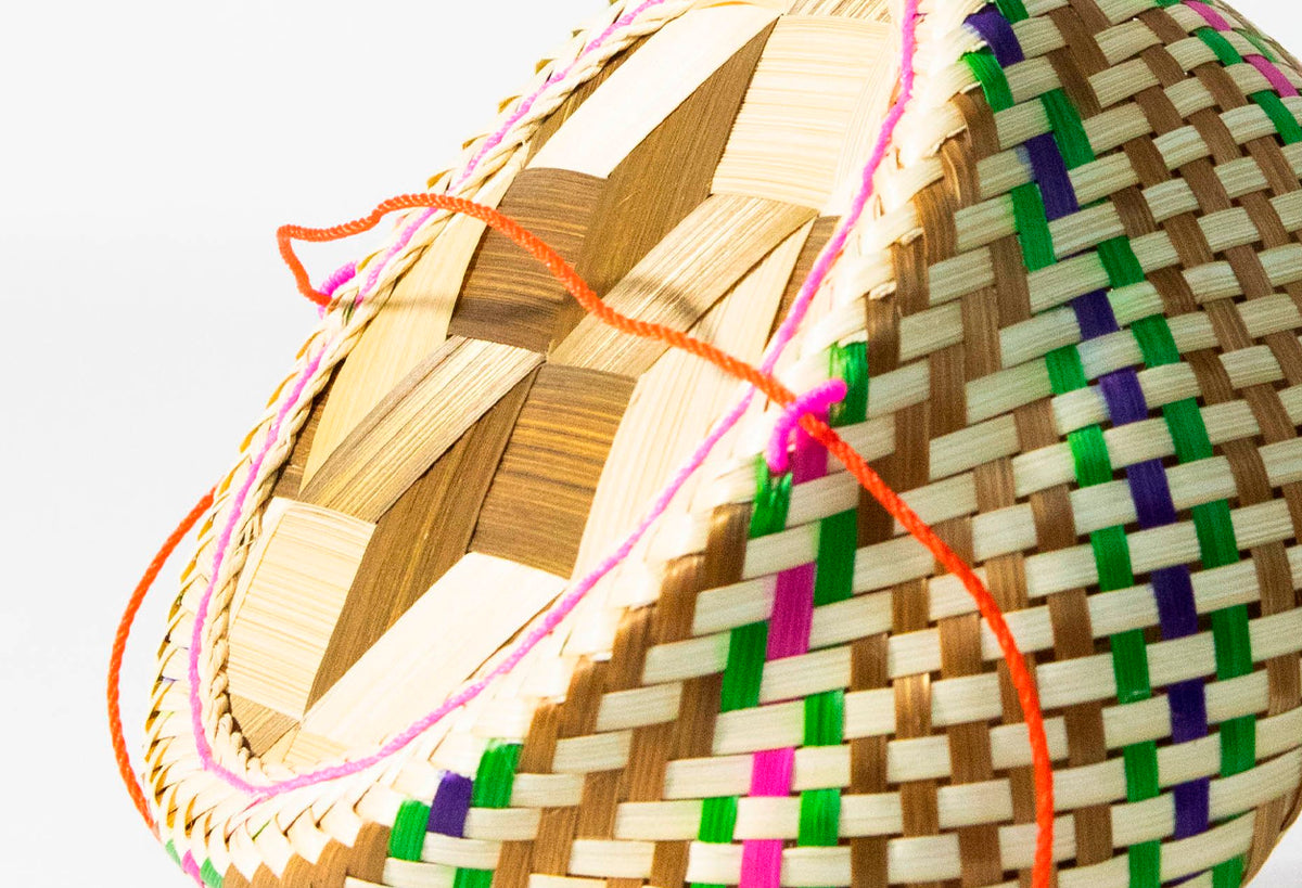 Woven bamboo basket with colorful geometric pattern and handles in orange, pink, and yellow rope.