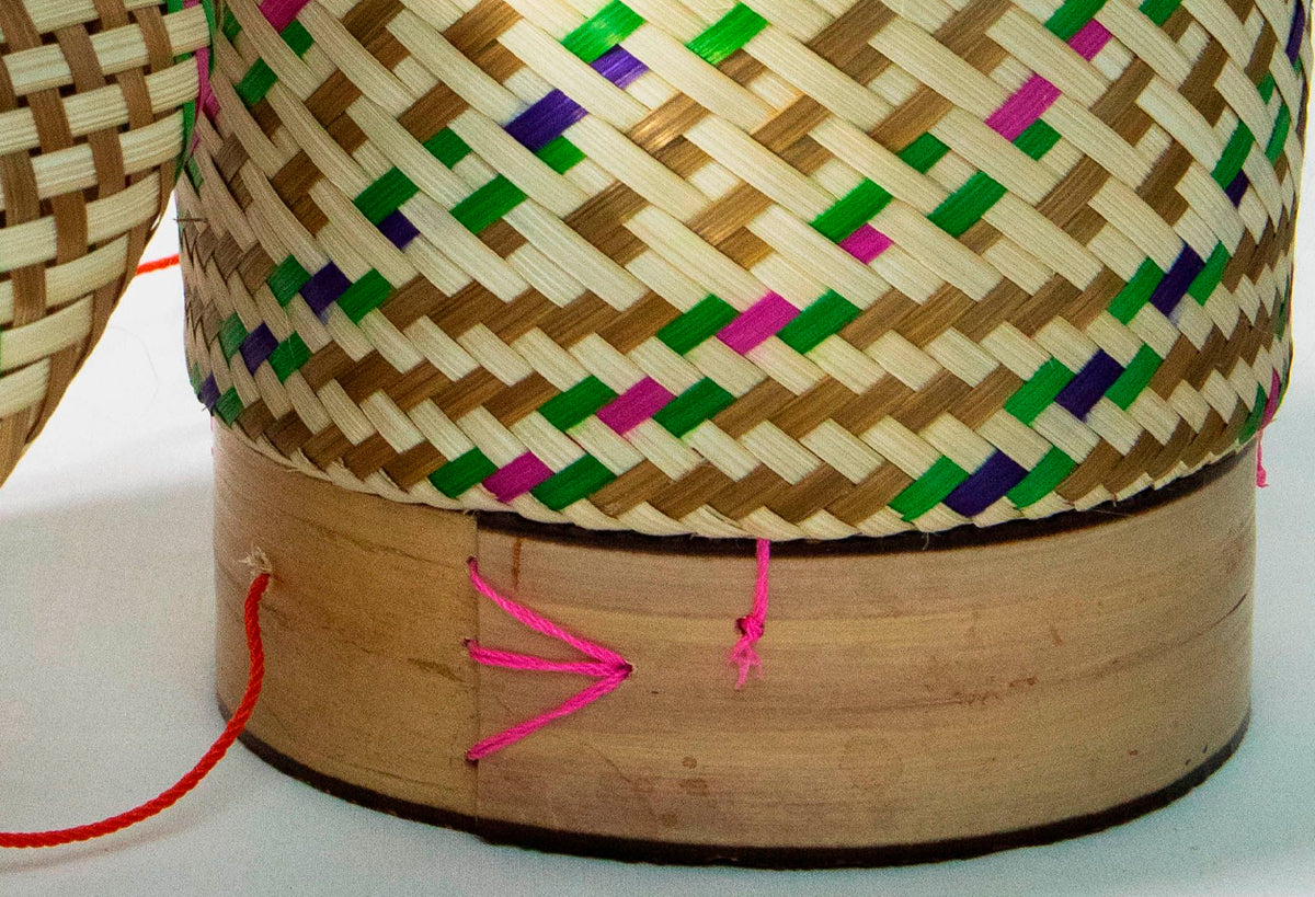 Woven bamboo rice basket with colorful geometric patterns in green, pink, and navy blue on natural tan weave.