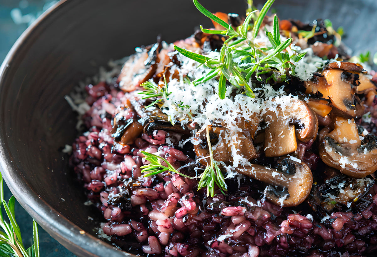 Dark purple riceberry rice cooked in a bowl with mushrooms, rosemary, and grated cheese.