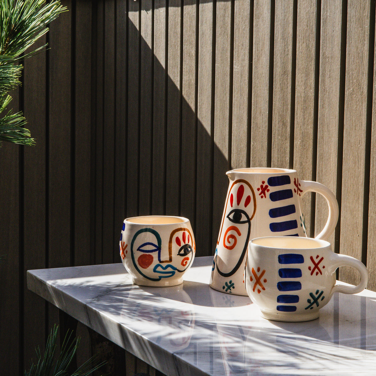 Two ceramic mugs with hand-painted abstract faces and geometric patterns in red, blue, and black on cream background.