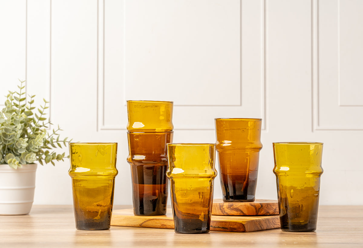 Six amber-colored Moroccan Beldi glasses with ribbed texture arranged on wooden coasters.