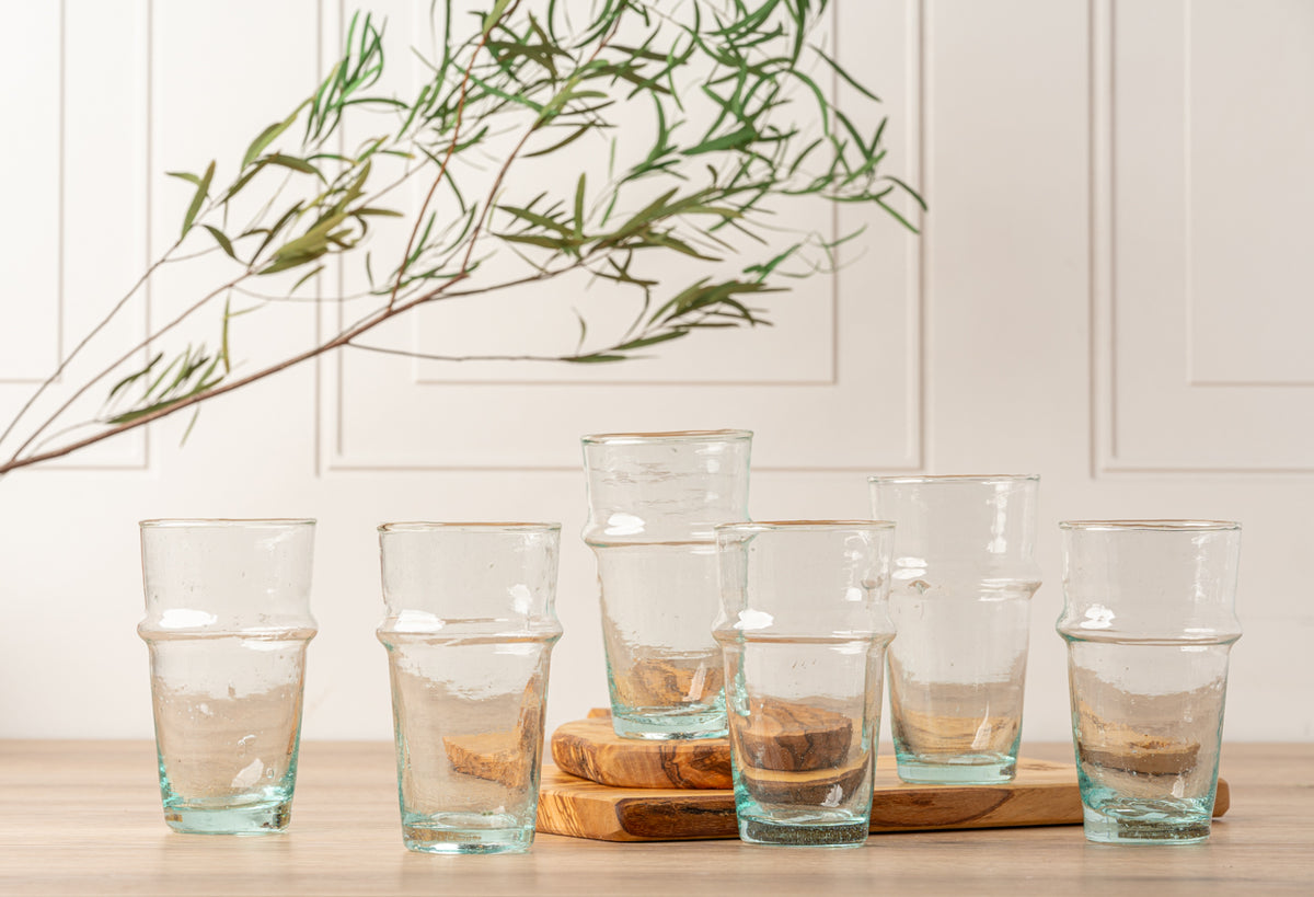 Six clear glasses with pale blue-tinted bases arranged in a row, some filled with amber liquid.