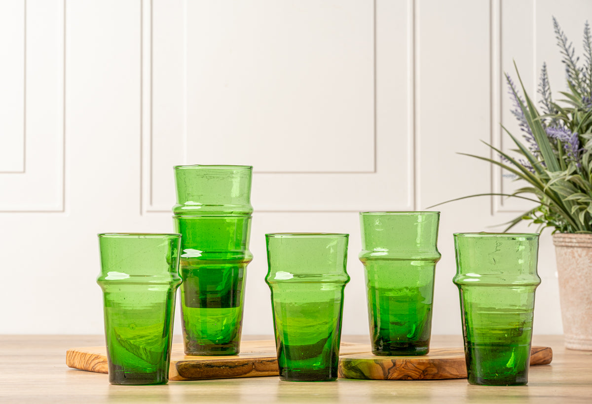 Six green Beldi glasses with textured surfaces and tapered shapes arranged on wooden bases.