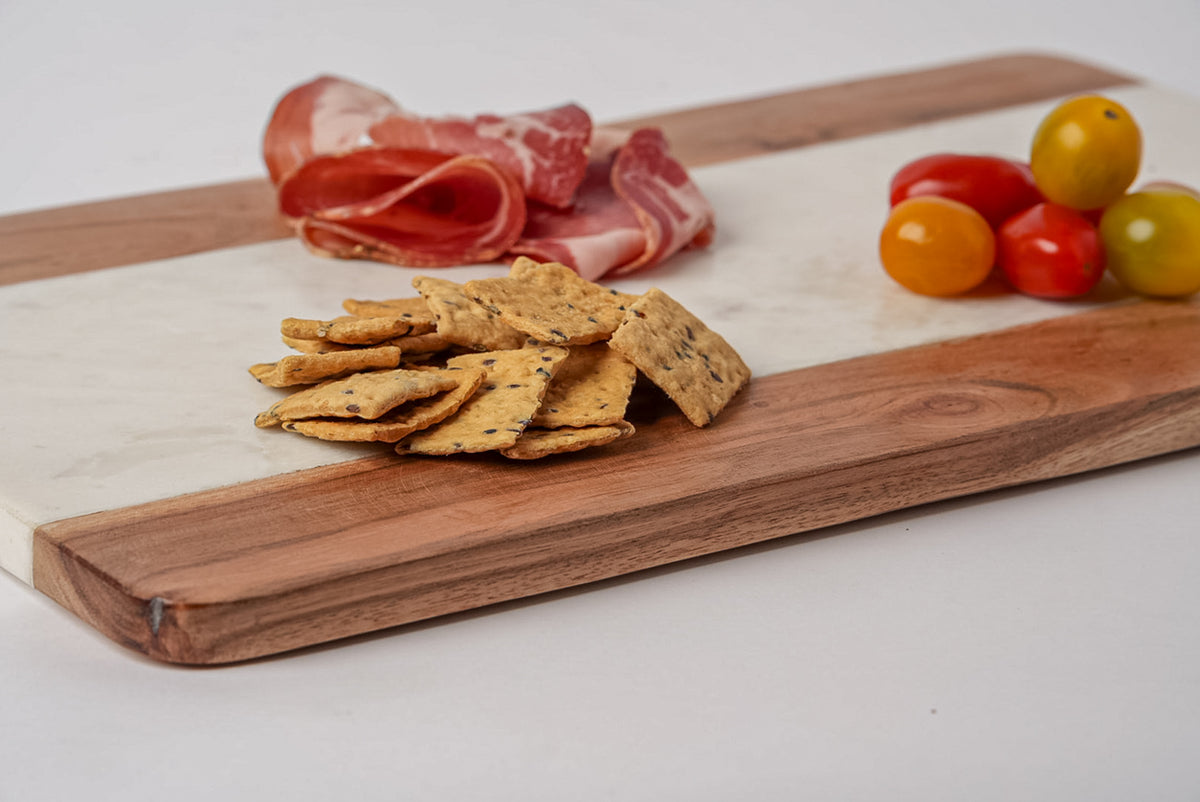 Rectangular serving board with white marble and light wood sections, displaying cured meats, crackers, and colorful olives.