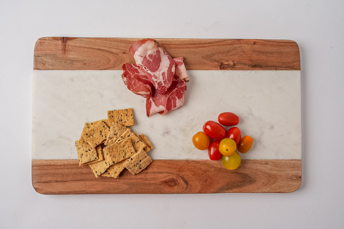 Rectangular serving board with acacia wood edges and white marble center, displaying cured meat, crackers, and cherry tomatoe