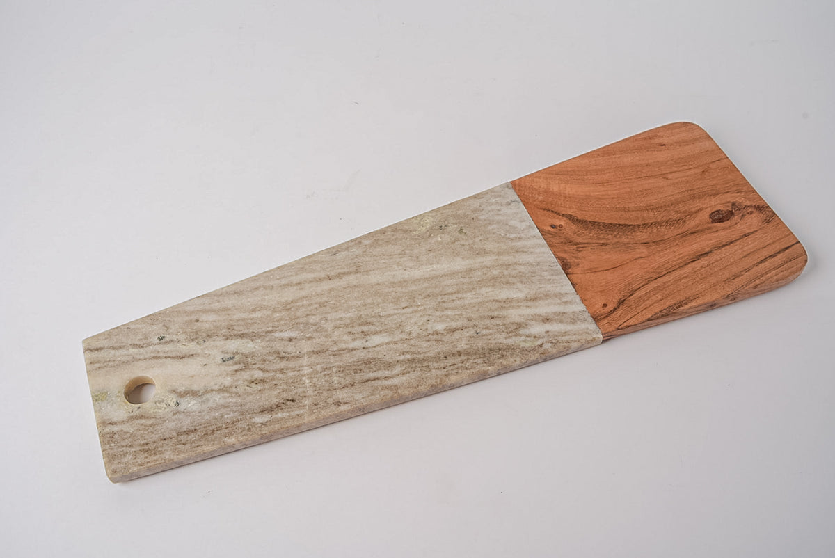 Long charcuterie board with tan marble section and acacia wood handle section, circular cutout on marble end.
