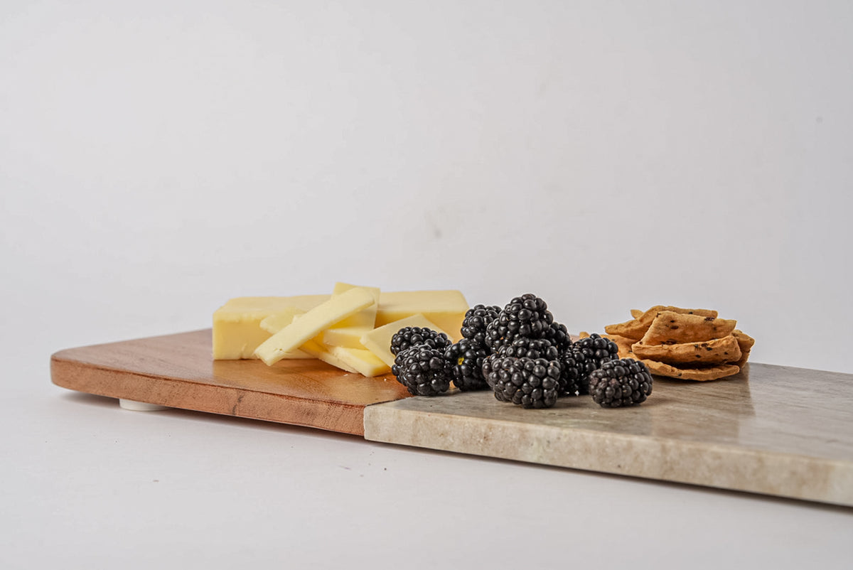 Long rectangular charcuterie board with tan marble and acacia wood sections, topped with cheese, berries, and crackers.