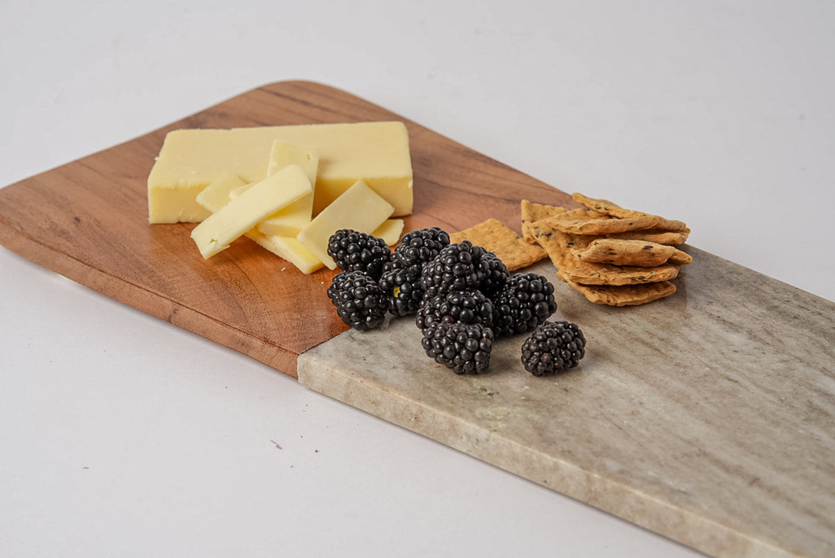 Long charcuterie board with acacia wood and marble sections, displaying cheese, crackers, and blackberries.