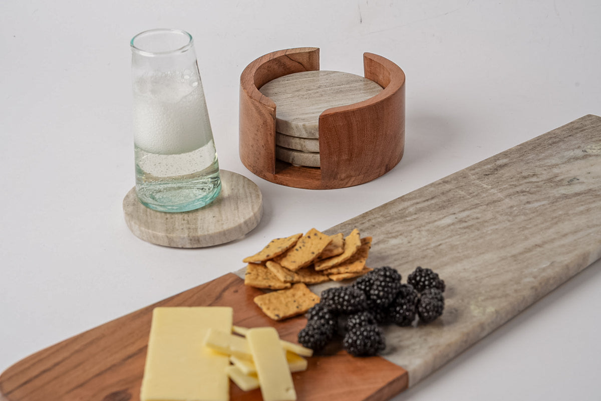Four tan marble coasters with wood holder, displayed with a glass and stacked in wooden caddy.