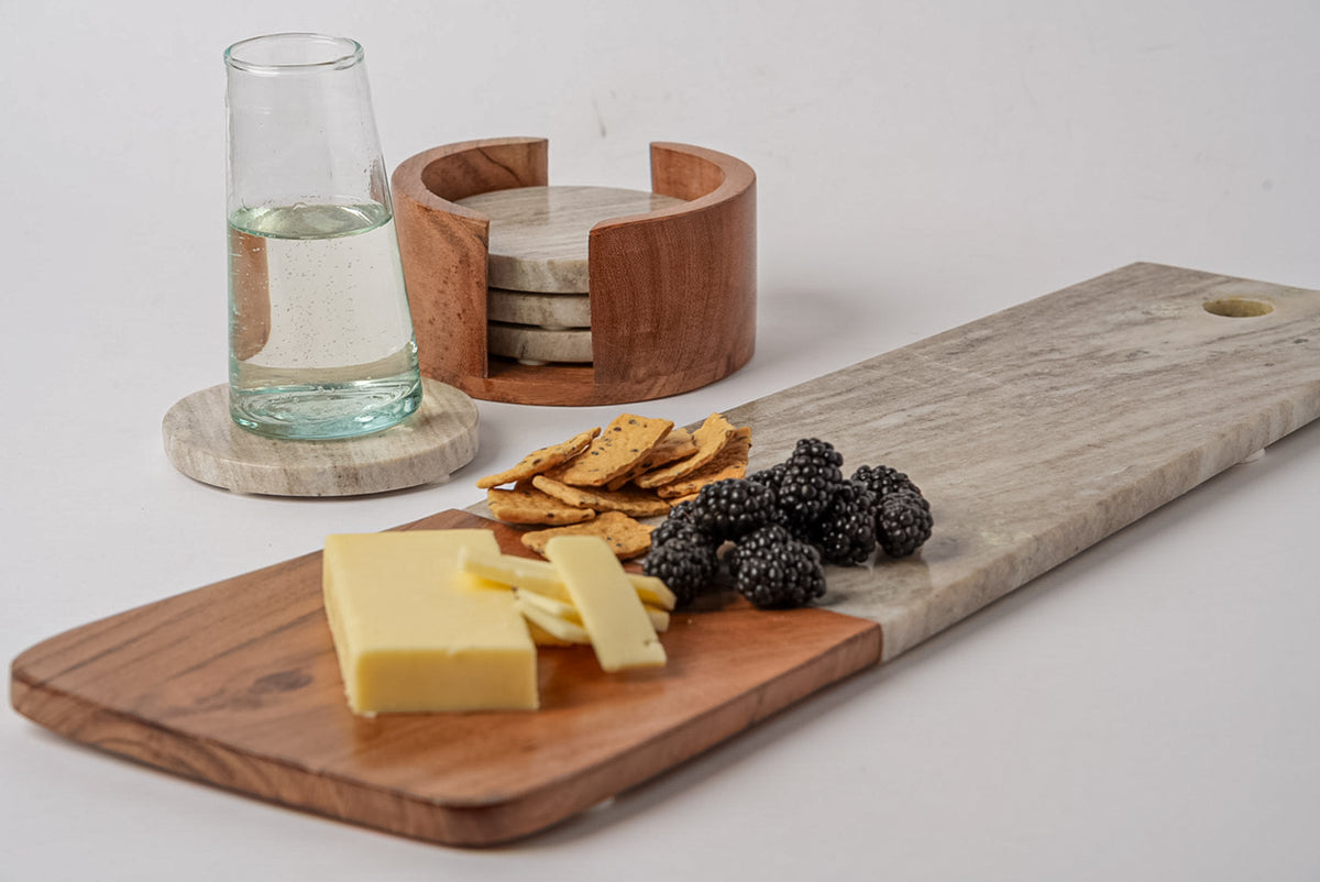 Long charcuterie board with tan marble and acacia wood sections, displaying cheese, crackers, and berries.