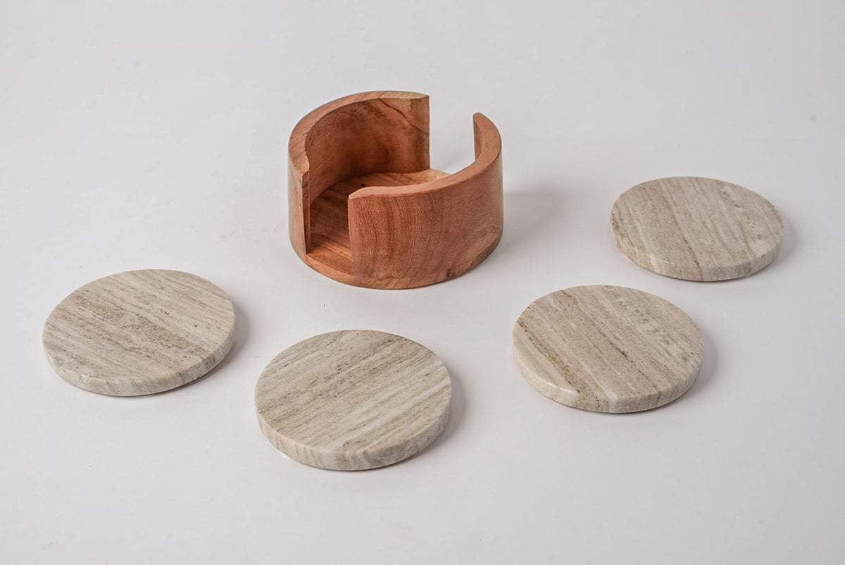 Four tan marble coasters with veined pattern and wooden holder with curved arms.