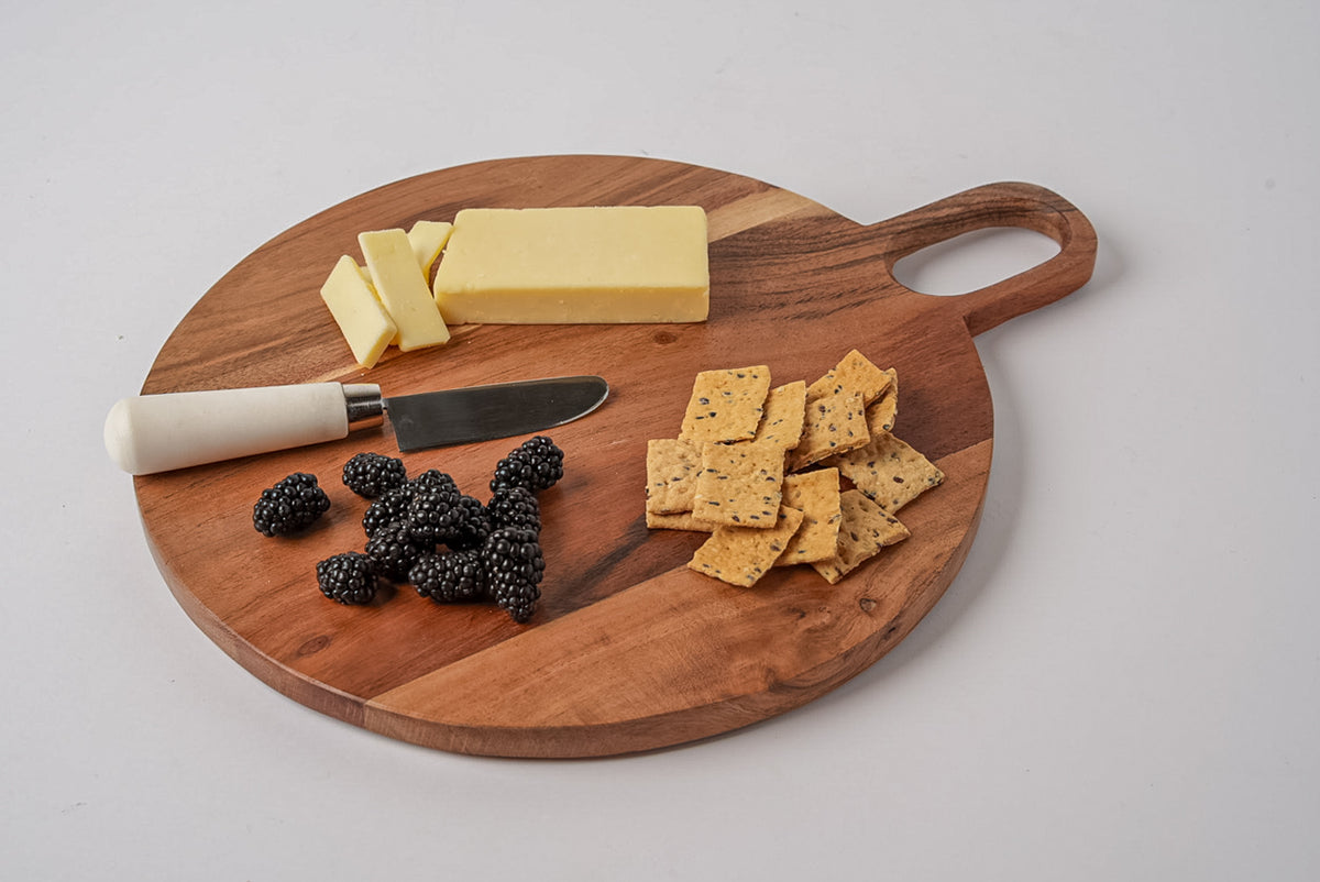 Round acacia wood serving board with handle, displaying cheese, crackers, berries, and a knife.
