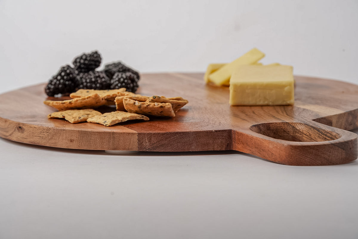 Round acacia wood serving board with handle, displayed with blackberries, crackers, and cheese.
