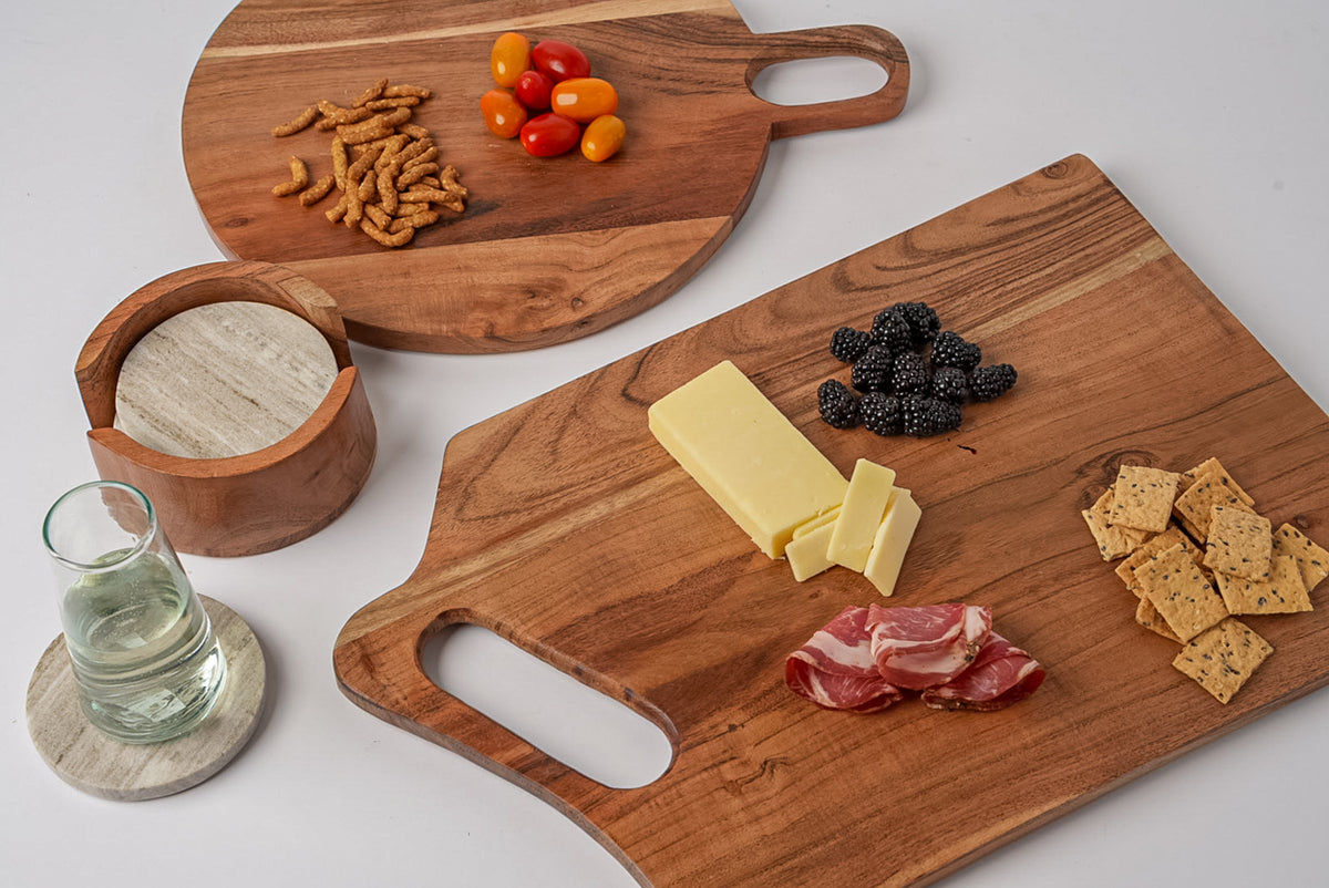 Rectangular acacia wood serving board with handle, displayed with cheese, crackers, berries, cured meat, and peppers.