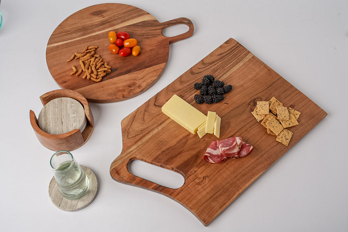 Round and rectangular acacia wood serving boards with handle cutouts, displayed with cheese, crackers, cured meat, berries, a