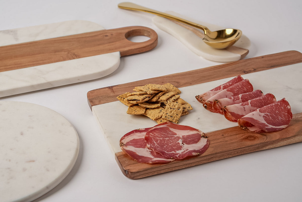 Rectangular serving board combining white marble and acacia wood sections, styled with cured meats and crackers.