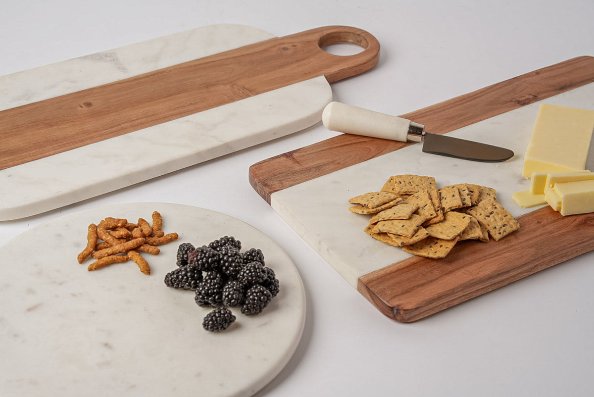 Wooden serving boards with circular handles, one with marble inlay, displayed with crackers, cheese, berries, and a knife.