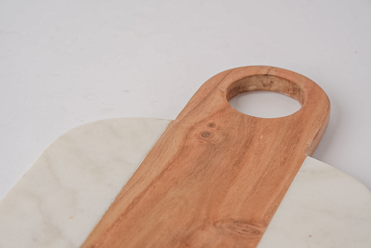 Wooden serving board with oval hole handle resting on white marble surface.