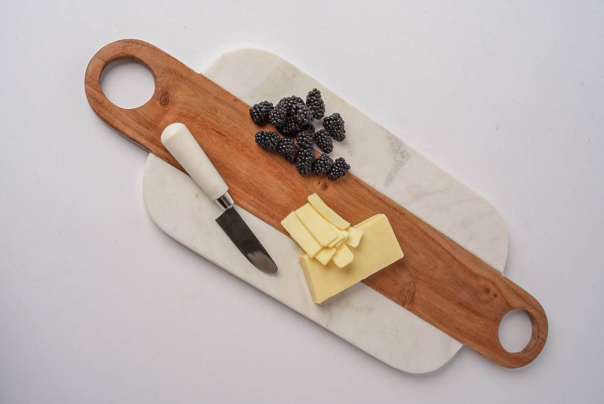 White marble and wood serving board with circular handles, topped with blackberries, cheese, and a knife.