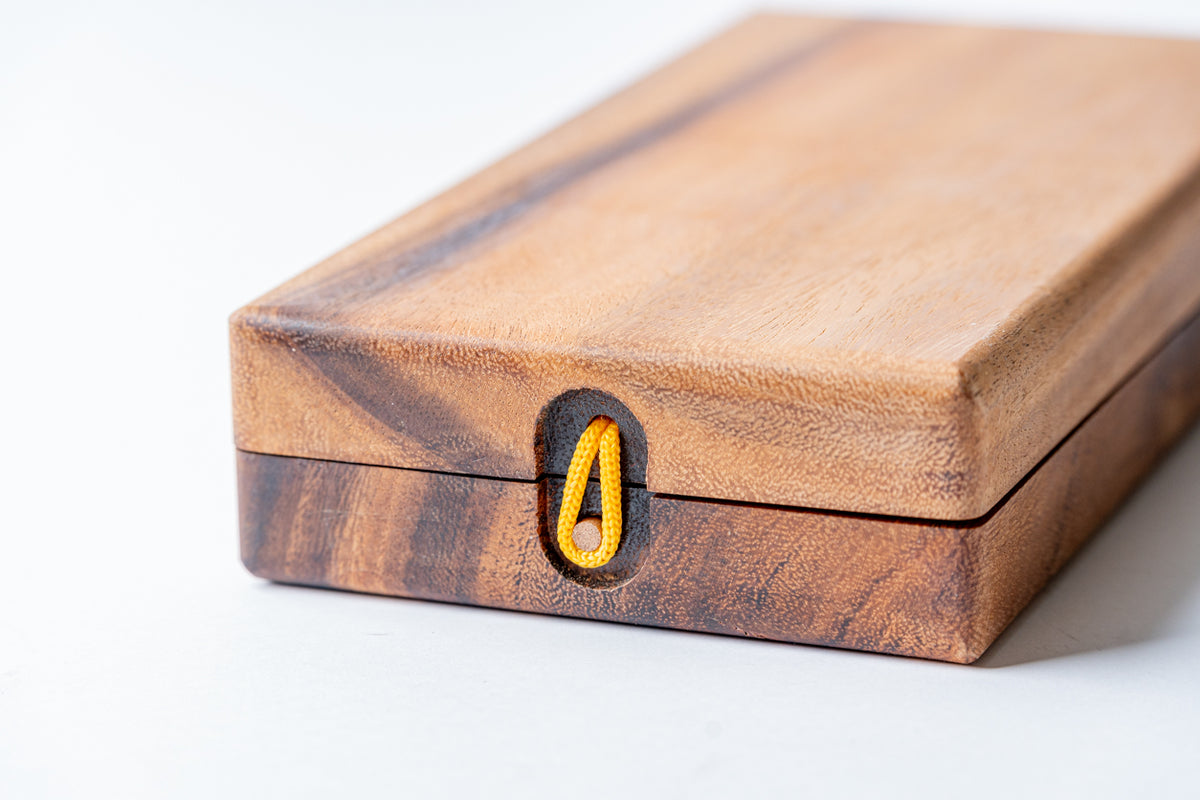 Wooden mancala board with hinged storage compartment and yellow game piece visible in center cup.