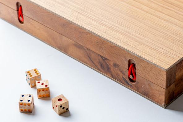 Wooden backgammon board with red handles and scattered dice showing various numbers on white surface.