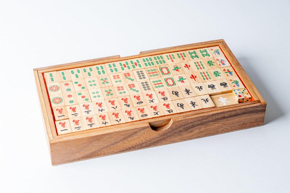 Mahjong game set in wooden box with carved tiles featuring Chinese characters and symbols arranged in rows.