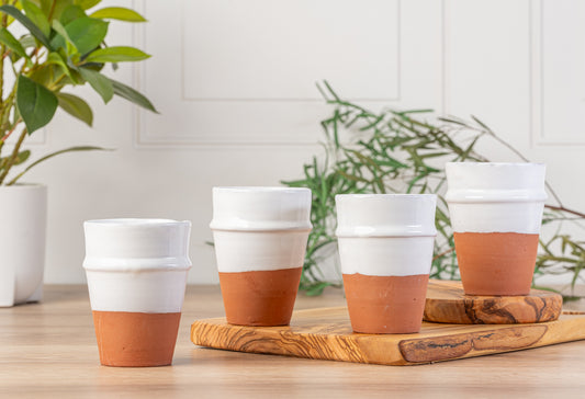 Four white ceramic cups with terracotta-colored bases and white bands arranged on a wooden tray.
