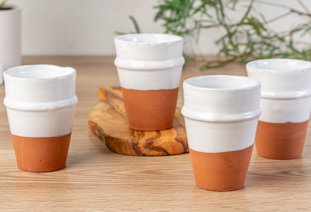 Four white ceramic cups with terracotta-colored lower sections and ridged rims, displayed on wooden surface with coasters.