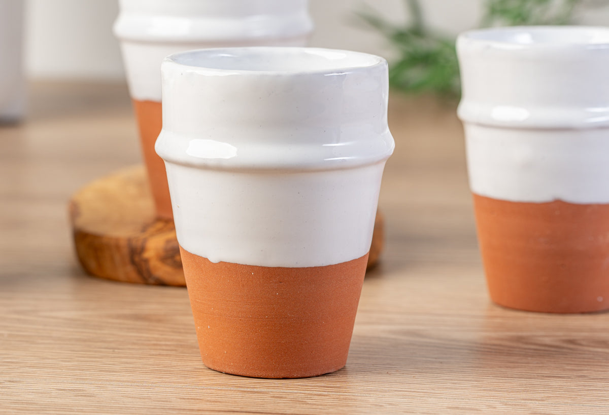 Four white ceramic cups with terracotta-colored lower sections and raised bands, arranged on a wooden surface.