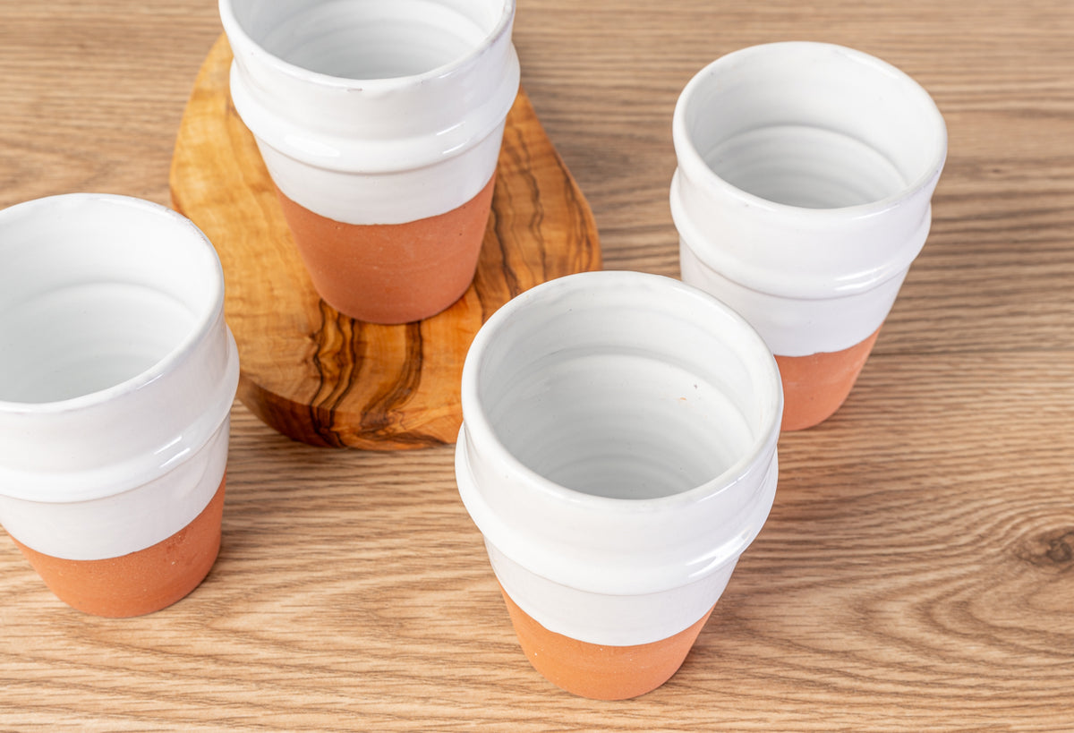 Four white ceramic cups with terracotta-colored lower sections arranged on a wooden surface.