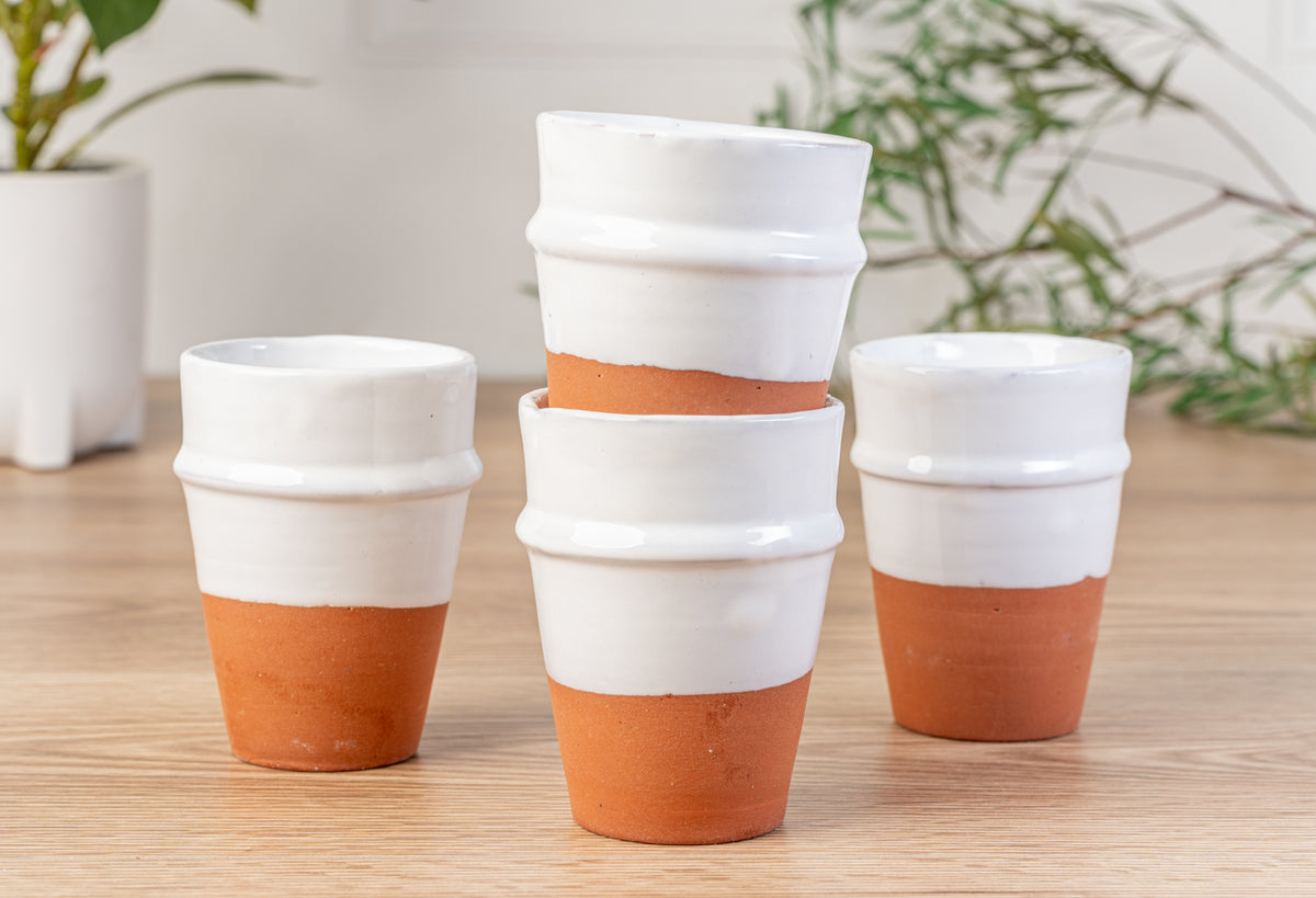 Four white ceramic cups with terracotta-colored lower sections and raised rim details, arranged on a wooden surface.
