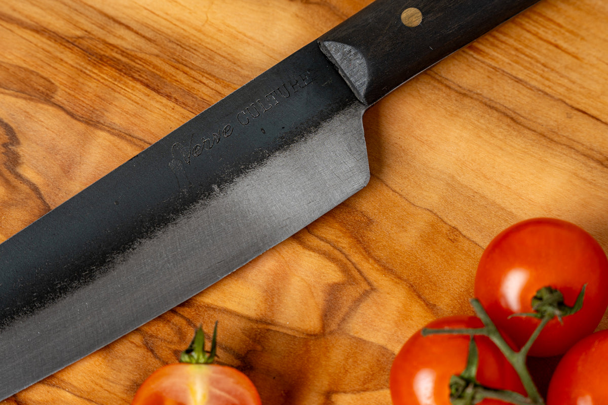Thai knife with dark blade and black handle on wooden cutting board next to fresh tomatoes.