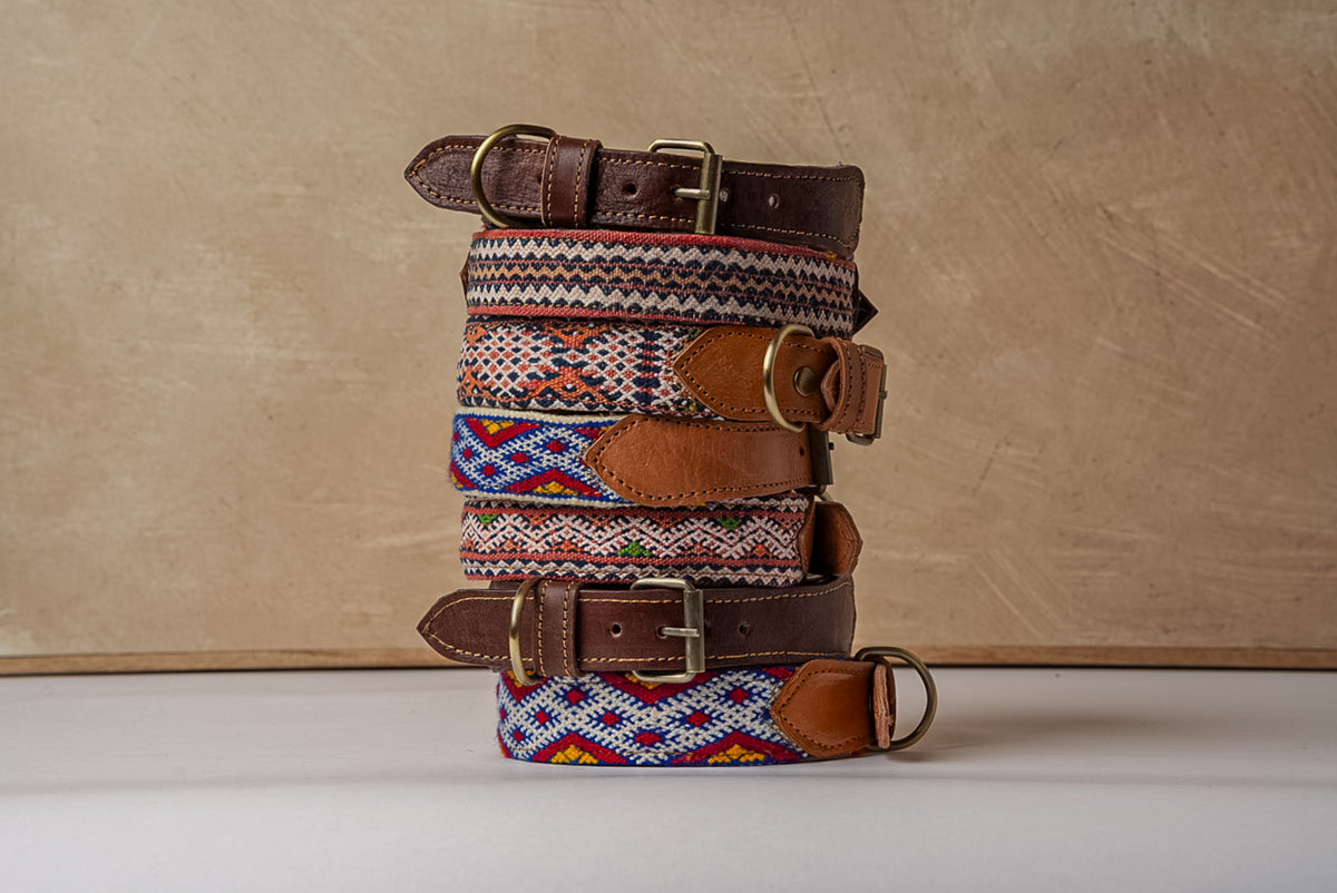 Stack of seven dog collars with woven kilim patterns, leather trim, and metal buckles in various color combinations.