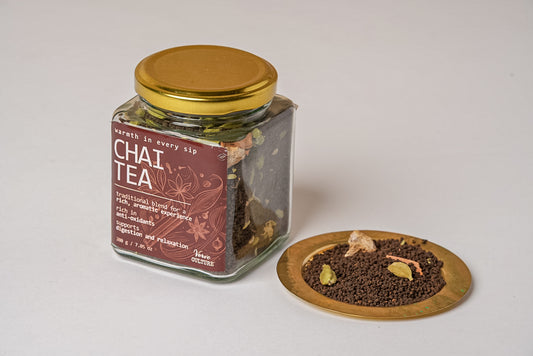 Glass jar with gold lid containing whole chai tea spices, displayed with contents on wooden plate.