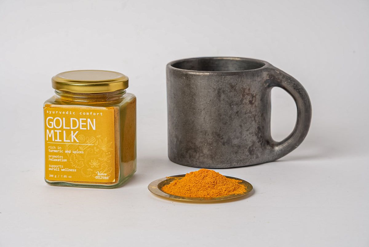 Golden Milk Spice Blend in glass jar with gold lid, dark ceramic mug, and golden powder on brass spoon.